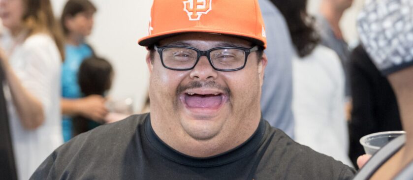 Close up of a man wearing an orange hat and glasses captured mid laugh.