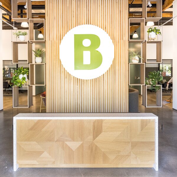 An interior shot of the Becoming Independent headquarters. Centered is a wooden slat wall with the BI logo symbol in green placed over a white circle.